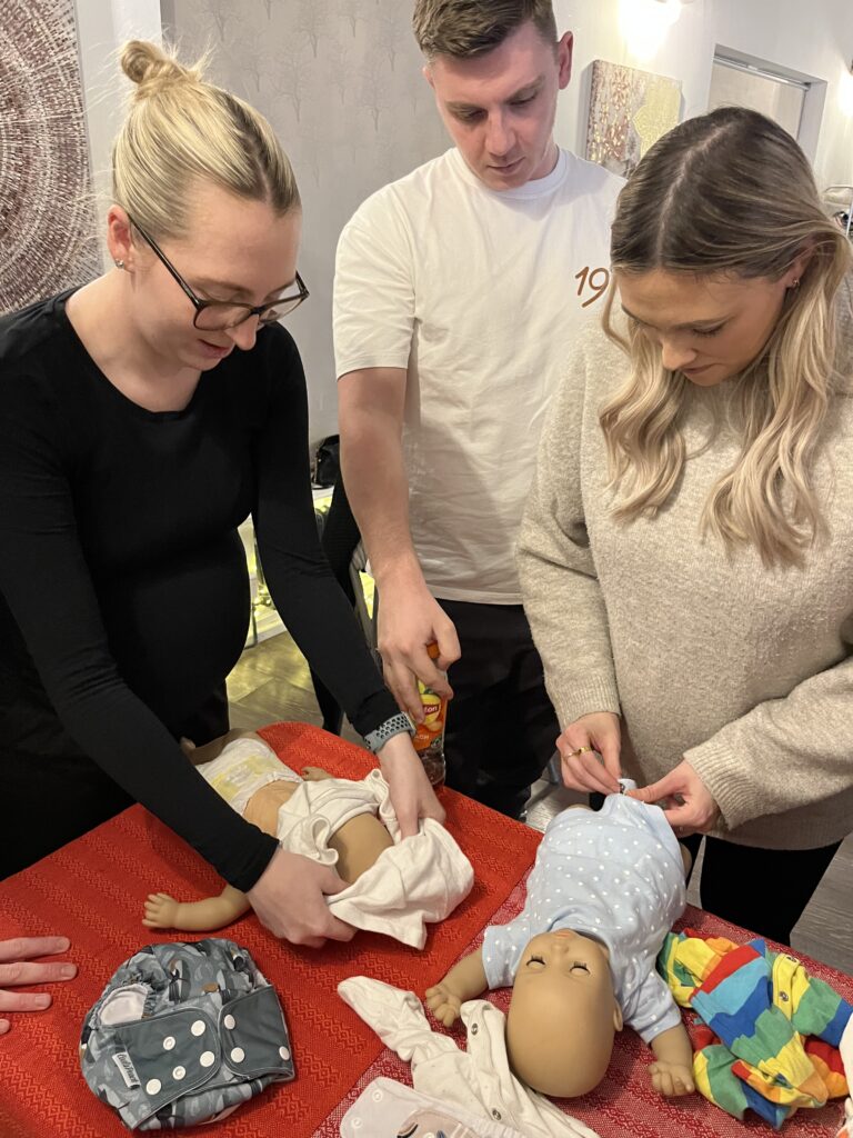 expectant parents learning how to change a nappy and dress a baby